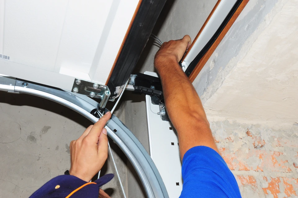 Intérieur de garage, technicien en bleu installant ou réparant un système de porte de garage sectionnelle