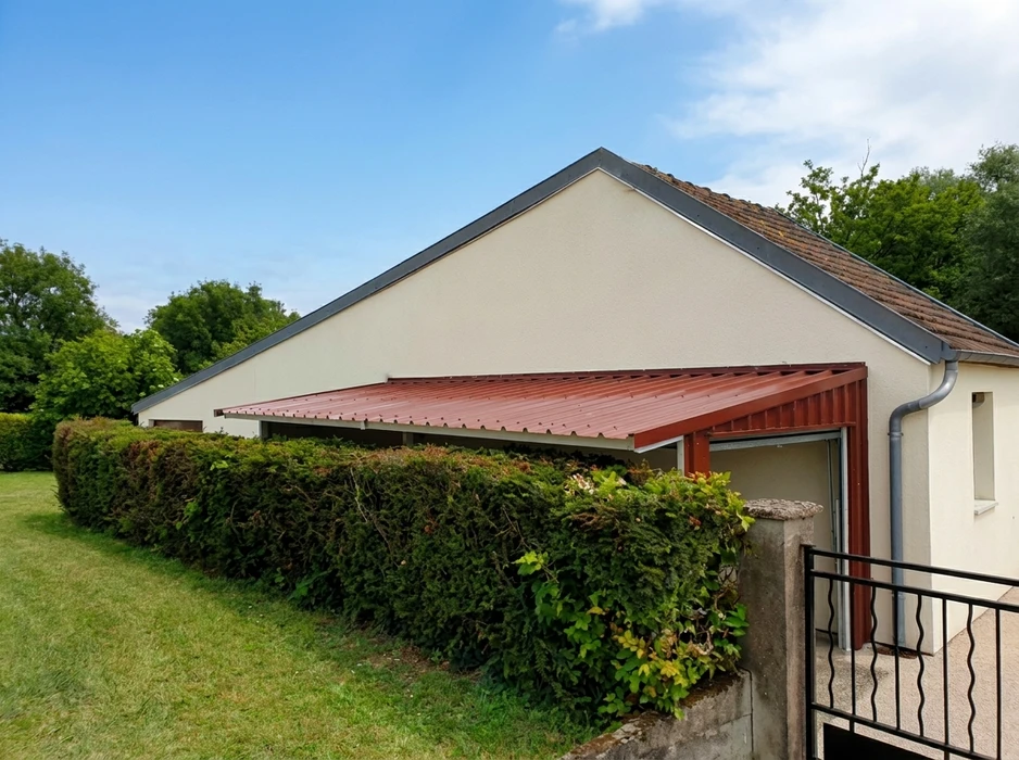Extension de maison avec auvent en bac acier rouge brique, fixé sur ossature métallique tubulaire, adossé au pignon d'un pavillon en enduit blanc