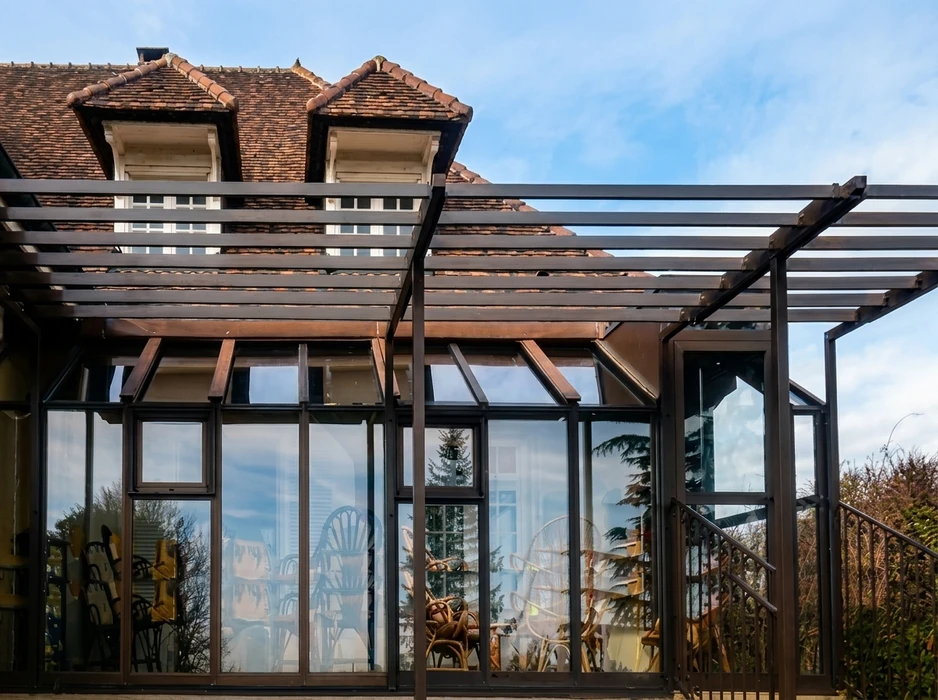 Véranda en acier thermolaqué noir mat, structure aluminium à vitrage simple, toiture mixte : verrière à pan coupé et pergola à lames orientables