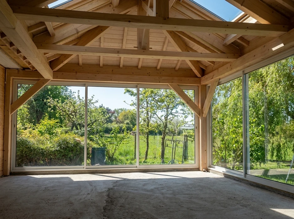 Intérieur d'une véranda en ossature bois, non meublée, avec vue sur jardin arboré