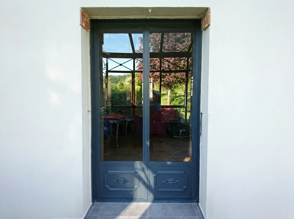 Porte-fenêtre double vantail en aluminium laqué gris anthracite, avec vitrage transparent et panneaux inférieurs moulurés décorés