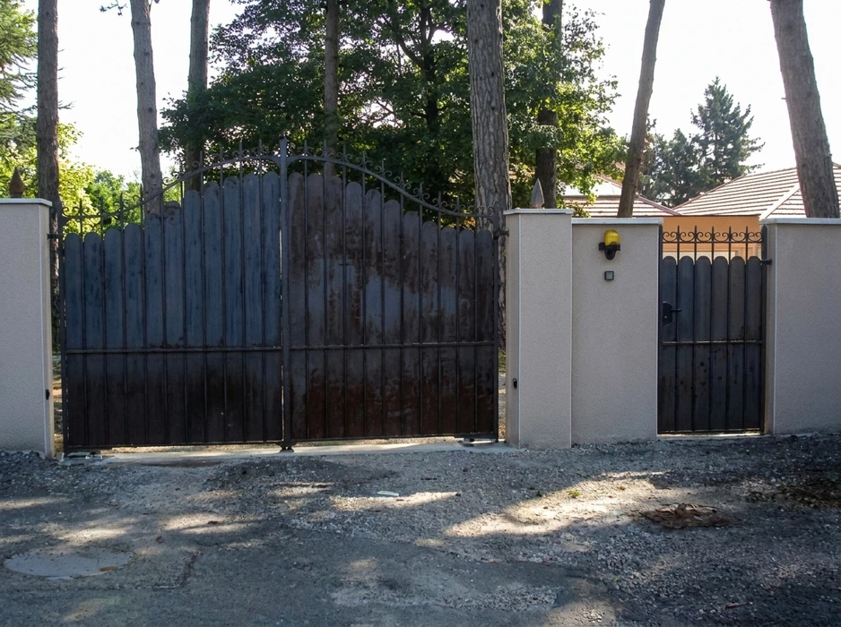 Entrée de propriété avec portail double battant en métal noir à lames verticales et décor en fer forgé avec volutes