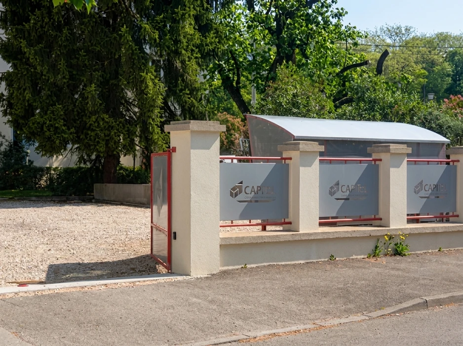 Entrée d'un site professionnel avec portail coulissant rouge et clôture basse en béton enduit