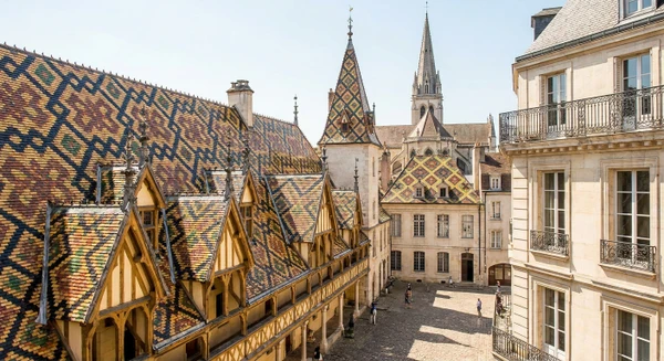 Photographie professionnelle d'une vue caract&eacute;ristique de Beaune&nbsp;: la basilique Notre-Dame ou les toits distinctifs avec leurs tuiles verniss&eacute;es color&eacute;es en motif de Bourgogne, prise depuis une perspective urbaine claire permettant d'identifier visuellement la ville. L'image doit &ecirc;tre une photographie r&eacute;aliste de qualit&eacute; professionnelle, claire et accueillante, montrant l'architecture et le contexte urbain embl&eacute;matique de Beaune.