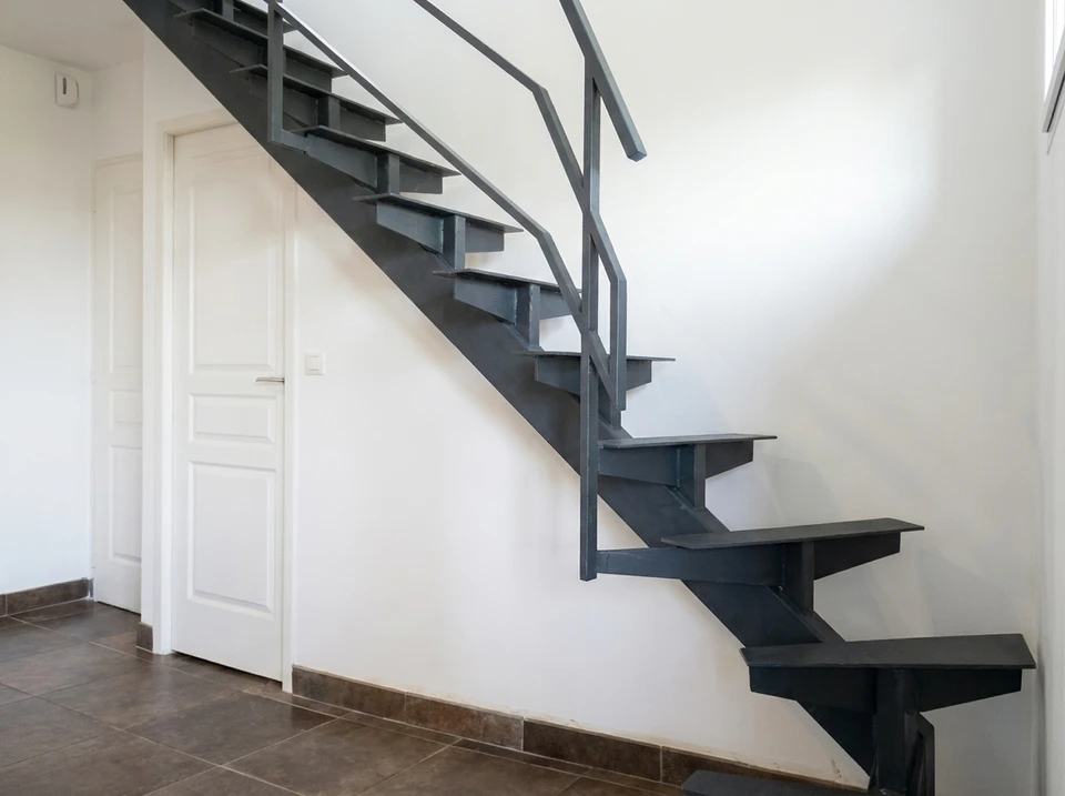 Artisan en tenue de travail avec ceinture porte-outils procède à l'installation d'un escalier industriel dans un intérieur moderne