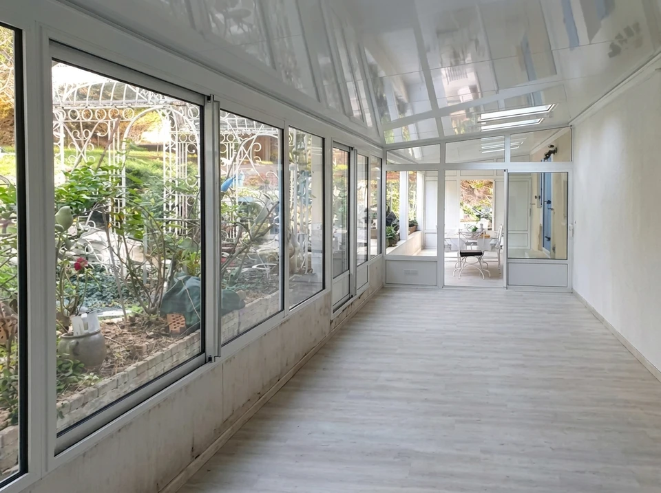 Véranda moderne avec grandes baies vitrées donnant sur paysage rural vallonné