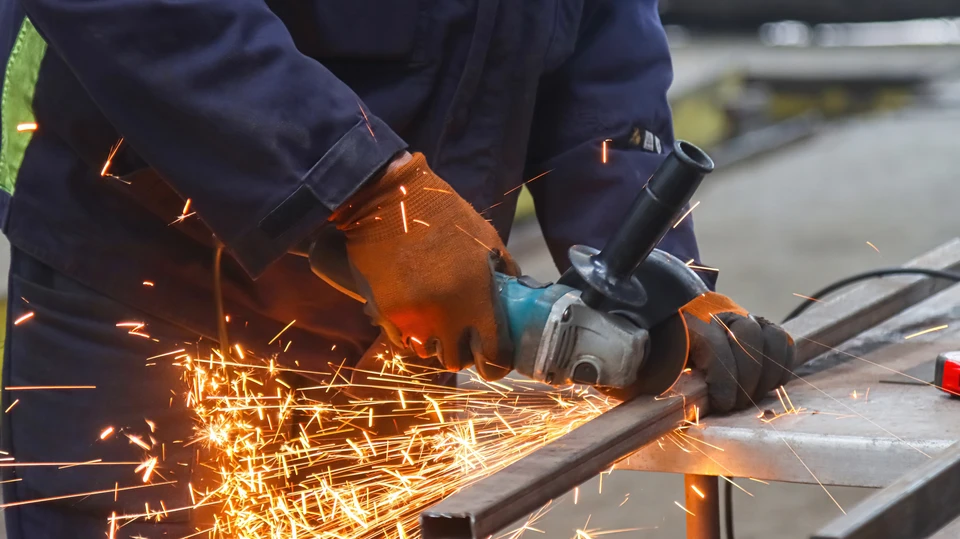 Soudeur professionnel travaillant dans un atelier industriel, portant un masque de protection et manipulant un chalumeau produisant des &eacute;tincelles intenses sur une pi&egrave;ce m&eacute;tallique